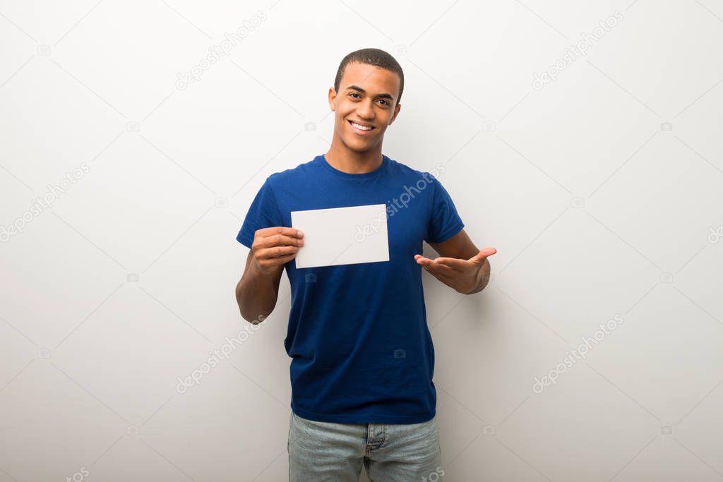 Young african american man on white wall holding an empty placard for insert a concept