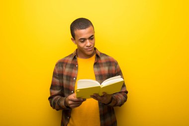 Bir kitap ve okuma zevk canlı sarı zemin üzerine genç Afro-Amerikan adam