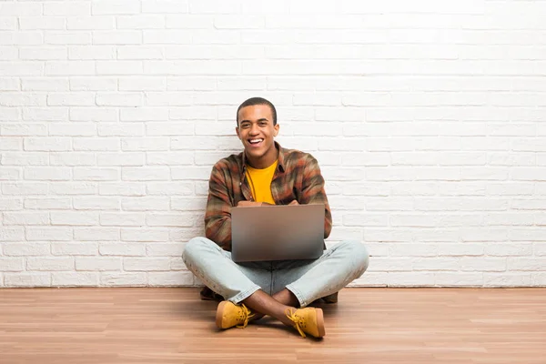 非洲裔美国人坐在地板上 他的笔记本电脑保持双臂交叉 而微笑 — 图库照片