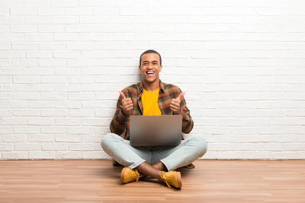 非洲裔美国人坐在地板上 他的笔记本电脑用双手和微笑竖起大拇指 — 图库照片