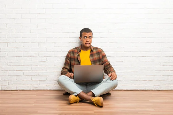 坐在地板上的非洲裔美国人拿着笔记本电脑有点紧张和害怕地按着牙齿 — 图库照片