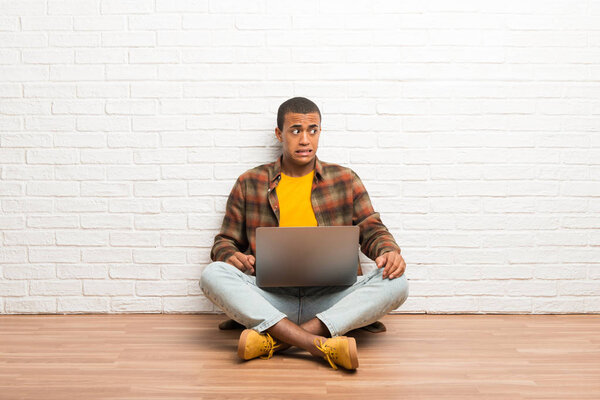 African american man sitting on the floor with his laptop is a little bit nervous and scared pressing the teeth