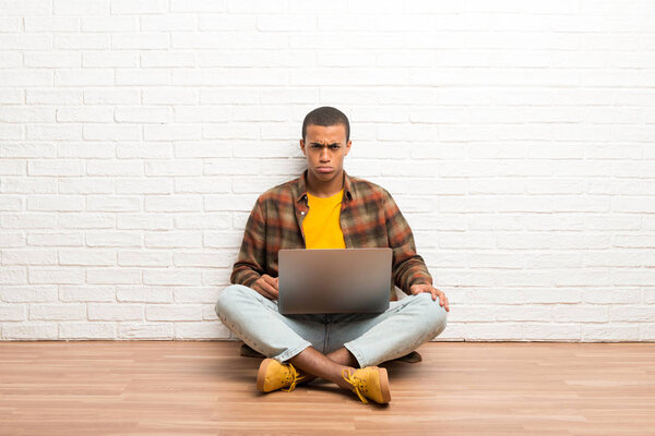 African american man sitting on the floor with his laptop with sad and depressed expression