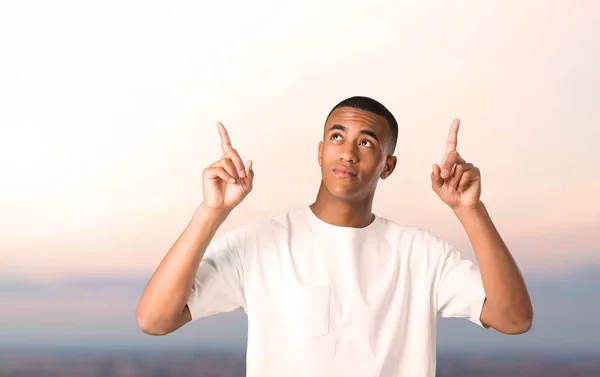 Young african american man pointing with the index finger a great idea and looking up on sunset background