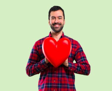 Yakışıklı adam yeşil arka plan üzerinde tutmak büyük kalp simgesi oyuncak