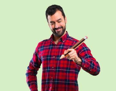 Yeşil arka plan üzerinde büyük bir kalem tutan yakışıklı adam