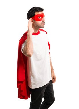 Süper kahraman maske ve kırmızı pelerin için bir şey kulak izole beyaz zemin üzerine elini koyarak dinleme adamla