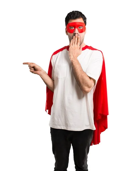 超级英雄男子与面具和红色斗篷指指点点的手指在一边 并提出了一个产品与惊讶的脸 同时覆盖在孤立的白色背景嘴 — 图库照片