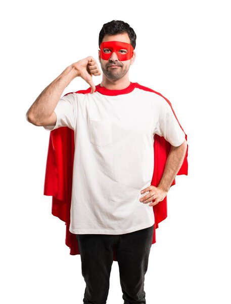 Superhero man with mask and red cape showing thumb down sign with negative expression. Sad expression on isolated white background