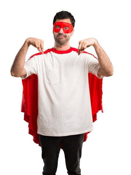 Superhero man with mask and red cape pointing down with fingers on isolated white background