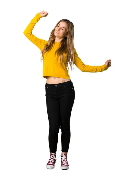 一个穿着黄色毛衣的年轻女孩在一个孤立的白色背景下听音乐时喜欢跳舞的全长照片 — 图库照片