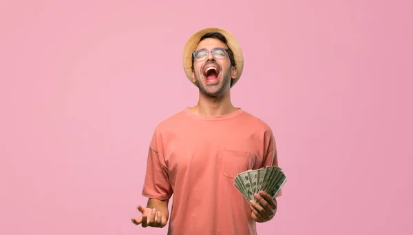 男子拿着许多钞票对着前面喊 嘴巴张大 背景是粉红色的 — 图库照片