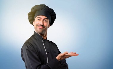 Şef adam siyah üniformalı bir ürün ya da bir fikir görünümlü doğru mavi arka plan üzerinde gülümseyen süre sunulması