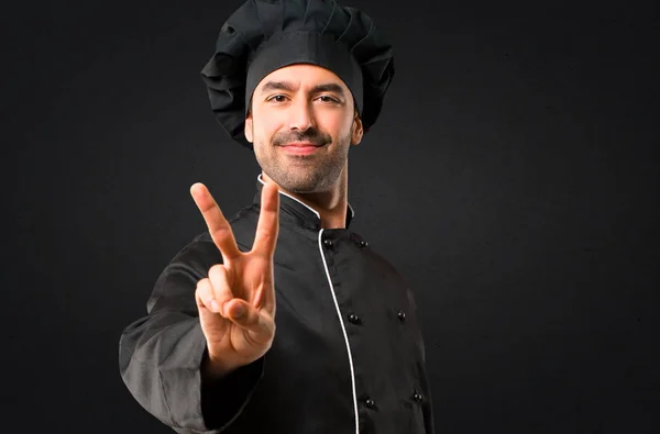 Chef Hombre Uniforme Negro Sonriendo Mostrando Signo Victoria Sobre Fondo —  Fotos de Stock