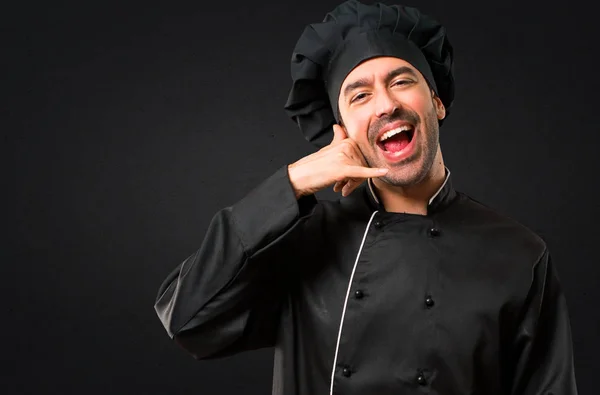 Chef man In black uniform making phone gesture and speaking with someone. Call me back sign on black background