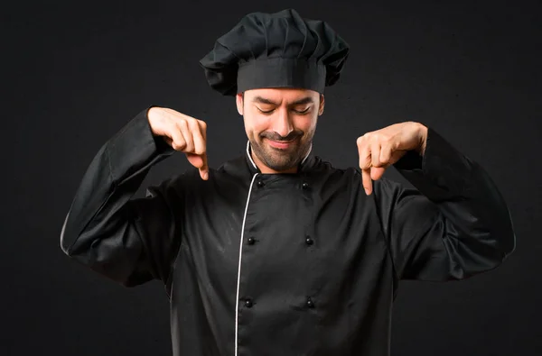 Chef man In black uniform pointing down with fingers on black background