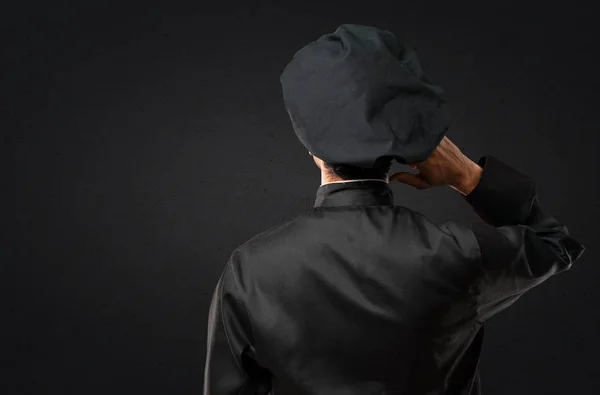 Chef man In black uniform on back position looking back while scratching head on black background