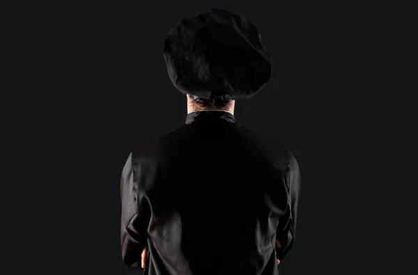Chef man In black uniform in back position on black background