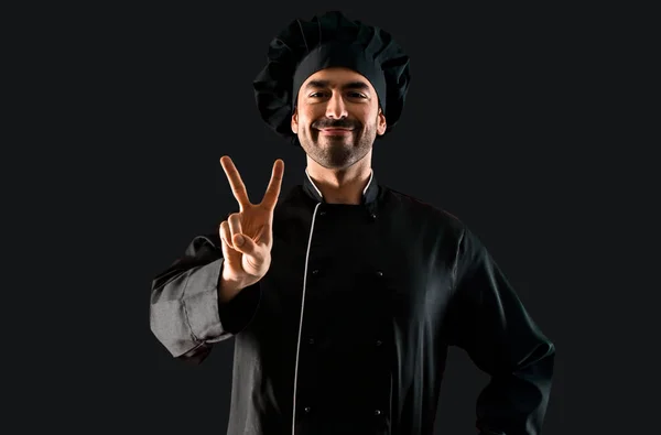 Chef Hombre Uniforme Negro Sonriendo Mostrando Signo Victoria Sobre Fondo —  Fotos de Stock