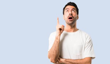 Genç adamla ayakta ve izole mavi arka plan üzerinde parmak işaret bir fikir düşünce beyaz gömlek