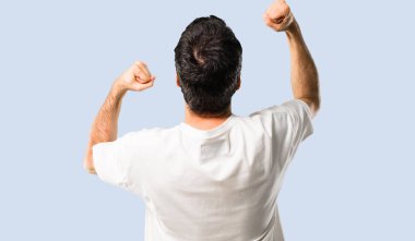 Genç adam ile beyaz gömlek bir zaferini kutluyor ve izole mavi arka plan üzerinde başarılı olmak için sürpriz