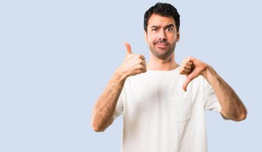 Beyaz gömlek iyi-kötü işaret yapma genç adam. Kararsız kişi Evet arasında veya izole mavi arka plan üzerinde değil