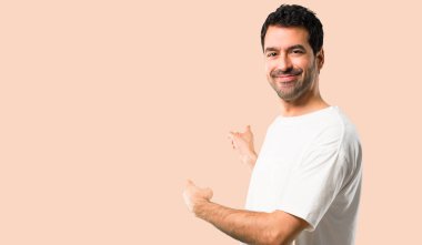 Beyaz gömlek geri bir ürün arkadan izole koyu sarı arka plan üzerinde sunulması işaret parmağı ile işaret ile genç adam