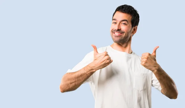 穿着白衬衫的年轻人竖起大拇指 面带微笑 因为在孤立的蓝色背景下取得了成功 — 图库照片