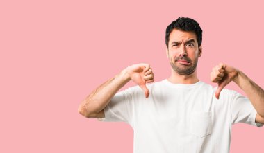 Başparmak aşağı her iki el ile gösterilen beyaz gömlek olan genç adam. Negatif ifade izole pembe bir arka plan üzerinde