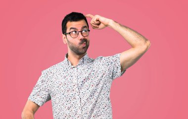 Yakışıklı adam gözlüklü şüpheleri ve pembe bir arka plan üzerinde karıştırmayın yüz ifadesi ile