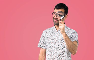 Pembe bir arka plan üzerinde büyüteç ile gözlüklü yakışıklı adam