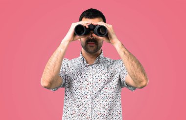 Pembe bir arka plan üzerinde dürbün ile gözlüklü yakışıklı adam