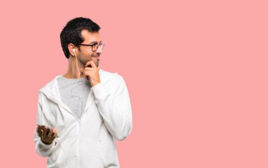 Adam gözlük ve ayakta ve çene üzerinde pembe bir arka plan üzerinde el ile tarafına bakarak müzik dinleme