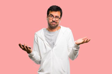 Adam gözlük ve müzik dinleme mutsuz ve bir şey ile sinirli çünkü bir şey anlamıyor. Pembe bir arka plan üzerinde negatif yüz ifadesi