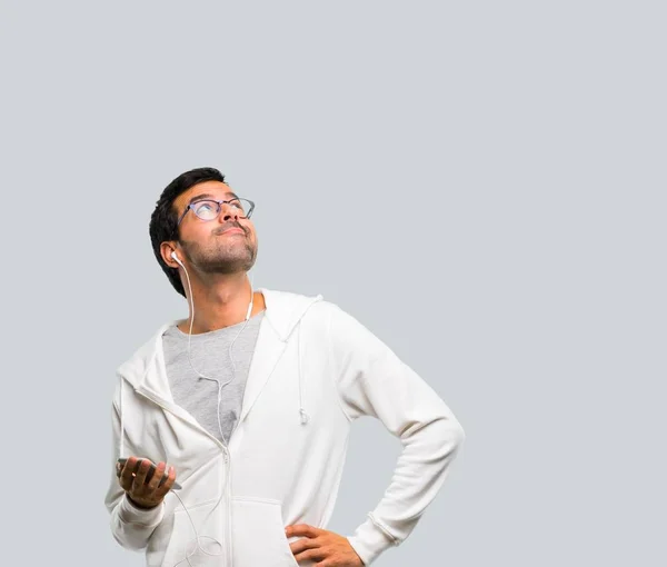 Man with glasses and listening music stand and looking up on grey background
