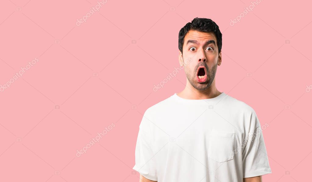 Young man with white shirt with surprise and shocked facial expression. Gaping because have just surprised with a gift on isolated pink background