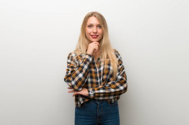 Sarışın genç kız gülümseyerek ve öne doğru emin yüz ile seyir beyaz duvar üzerinde