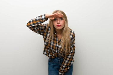 Bir şey bakmak için beyaz duvar uzakta el ile seyir üzerinde sarışın genç kız