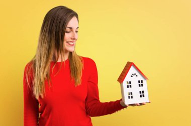 Sarı arka plan küçük bir ev tutan mutlu genç sarışın kadın