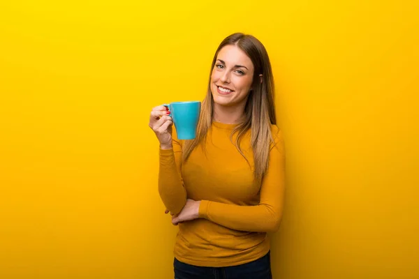 熱い一杯のコーヒーを保持している黄色の背景の若い女性 — ストック写真