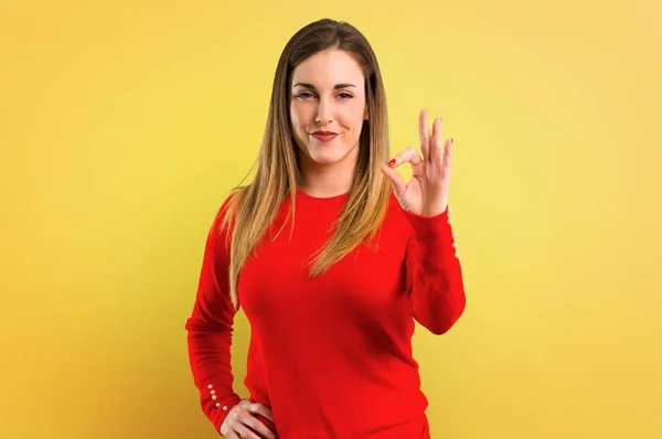 黄色の背景に指で のサインを示す若いブロンドの女性 — ストック写真