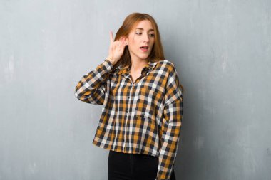 Genç Kızıl saçlı kız bir şey kulak el koyarak dinleme grunge duvarın üzerinden