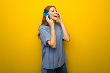 Sarı duvar arka plan kulaklık ile müzik dinlemek genç Kızıl saçlı kız