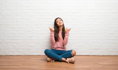 Her iki el ile jest Yaşasın vererek ve gülümseyen bir odada katta oturan genç kız