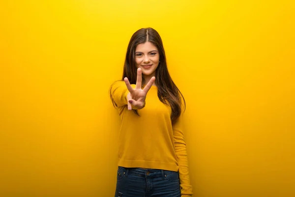 十几岁的女孩在充满活力的黄色背景高兴和计数三用手指 — 图库照片