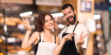 Gülümseyen ve zafer gösterilen aşçılar çift her iki el ile kayıt