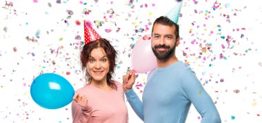 Balonlar ve kalça, silah ile poz ve konfeti bir parti ile gülümseyen Doğum günü şapka ile çift
