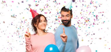 Balonlar ve gösterilen ve konfeti bir parti ile en iyi işareti parmak kaldırma Doğum günü şapka ile çift