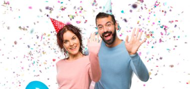 Balonlar ve konfeti bir parti ile mutlu ifade ile el ile selamlayan Doğum günü şapka ile çift