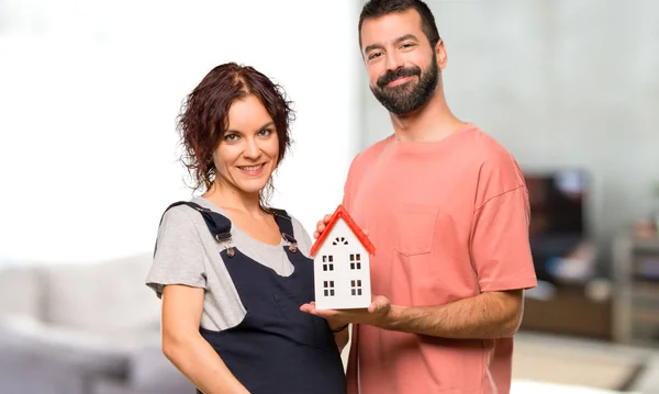 Casal Com Mulher Grávida Segurando Uma Pequena Casa Dentro Casa — Fotografia de Stock